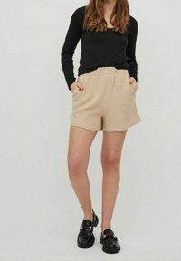 Beige texturované kraťasy s elastickým pasem a bočními kapsami, v kombinaci s černým topem s dlouhým rukávem a černými masivními botami.