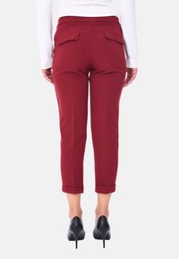 Pantaloni bordeaux a vita alta con una vestibilità slim, dotati di due tasche posteriori e orli arrotolati. Realizzati in un tessuto morbido, abbinati a tacchi alti neri.