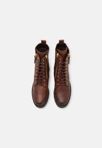 Botas de piel marrón hasta el tobillo con herrajes dorados, cordones en la parte delantera, cremalleras laterales y una suela texturizada, con un forro suave.