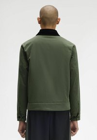Giacca verde oliva con colletto in corduroy, maniche lunghe, polsini con bottoni e una texture liscia. Presenta un design minimalista e una vestibilità sartoriale.