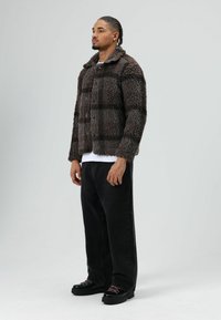 Gray faux fur jacket with a plaid pattern, button closure, and pointed collar. Paired with black baggy pants and chunky black shoes.