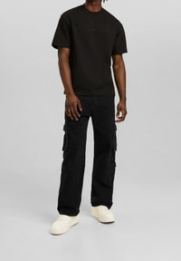 Czarny bawełniany t-shirt z okrągłym dekoltem, zestawiony z czarnymi spodniami cargo z bocznymi kieszeniami i luźnym krojem. Całość dopełniają białe trampki.