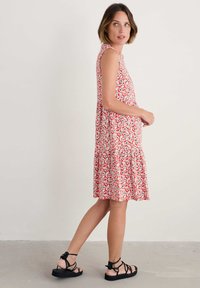 Rochie fără mâneci, roșie, cu tivuri volanate, realizată dintr-un material ușor, cu un model floral alb și negru. Sandale negre cu bretele.