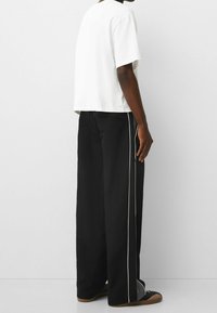 Vit bomullströja med korta ärmar, kombinerad med svarta byxor med vida ben som har vita sidopipningar och en bakficka. Avslappnad outfitvinkel.