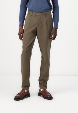 Olivenfargede bukser med rett snitt, laget av bomullsstoff. Har en enkelt knappelukking og frontfolder. Brukt med brune loafers.