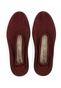 Zapatos de punto en color burdeos, tipo slip-on, con puntera redonda, suela flexible negra y parte superior texturizada. Incluyen una plantilla acolchada y bordes elásticos.