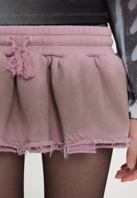 Pink gathered skirt with an elastic waistband, featuring textured fabric and raw hem details. Includes drawstring ties with tassels.