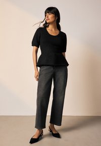 Fekete peplum felső rövid ujjal, magas derékú, laza fazonú sötét farmernadrággal és hegyes orrú fekete slingback cipővel párosítva.