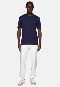 Navy short-sleeve t-shirt with a crew neckline and a chest pocket, paired with white joggers and white sneakers with beige accents.