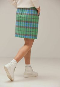 Vihreä ja sininen ruutukuosisellinen villahame, jossa on sivutaskut. Hameen leikkaus on suora ja kangas tuntuu selvästi pehmeältä. Hameen kanssa on yhdistetty valkoiset korkeat tennarit.