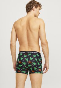 Boxer-briefs noirs avec des motifs de sapins de Noël verts festifs, accentués par du texte orange. La ceinture élastique présente le logo "JACK & JONES".