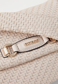 Sac à main tissé beige avec une texture lisse, orné d'un logo en or et d'accents en matériel doré. Conçu avec une fermeture à rabat.