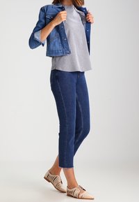 Kurtka dżinsowa, bluzka w paski, ciemnoniebieskie jeansy o kroju 7/8 oraz beżowe buty z wycięciami. Widoczne przeszycia na jeansach.