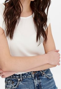 Vit kortärmad topp med en slät textur, kombinerad med högmidjade blå denimjeans med en blekt finish och slitna detaljer.