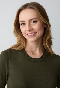 Olivgrüner Strickpullover mit rundem Halsausschnitt und geribtem Saum. Weiche Textur und taillierte Passform, die einen glatten, gleichmäßigen Stoff betont.