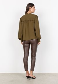 Olive green, long-sleeve blouse with pleated back, ruffled detail; paired with fitted brown faux leather pants and black heeled sandals.