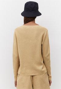 Beige värillinen pitkähihaisen toppi, jossa leveä pääntie. Yhdistetty tummansiniseen lierihattuun. Sileä kangas ja rento istuvuus.