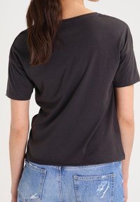 Camiseta de algodón negra con un corte relajado, mangas cortas y un cuello redondo, combinada con jeans de mezclilla desgastados en azul claro.