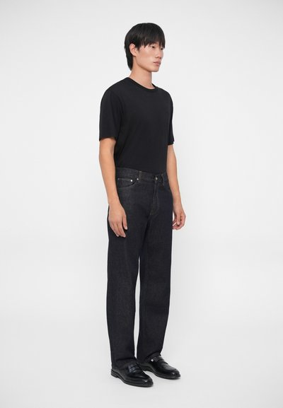 Camiseta negra de manga corta combinada con unos vaqueros de denim azul oscuro, con corte recto y detalles de costura sutiles. Unos zapatos negros completan el conjunto.