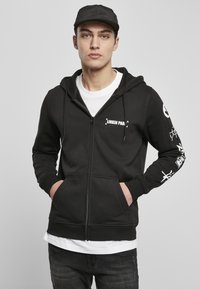 Sort zip-up hoodie lavet af en bomuldsblanding, med en kængurulomme, hvid "Linkin Park" logo, og grafiske designs på ærmerne.