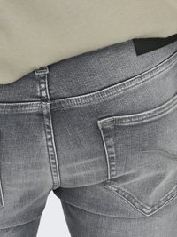 Gros plan d'une personne portant un jean gris délavé avec des coutures visibles et des poches arrière, associé à un haut beige clair.