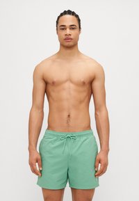 Shorts de baie verzi cu talie elastică și șnur de ajustare. Material neted, lungime până deasupra genunchiului, fără modele sau accente vizibile.