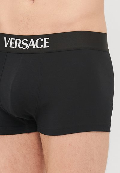 Schwarze Boxershorts aus glattem Stoff. Verfügt über einen breiten elastischen Bund mit dem Aufdruck "VERSACE" in weißer Schrift. Figurbetontes Design.