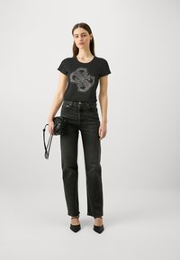 Camiseta negra con un diseño gráfico de strass, combinada con jeans oscuros de cintura alta y tacones negros de punta. Los accesorios incluyen un bolso pequeño.