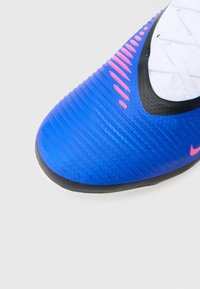 Μπλε ποδοσφαιρικό παπούτσι με υφασμάτινο σύνθετο επάνω μέρος με υφή, ροζ ριγέ διακριτικά, μαύρες λεπτομέρειες γύρω από το άνοιγμα και λαστιχένια σόλα για καλύτερη πρόσφυση.