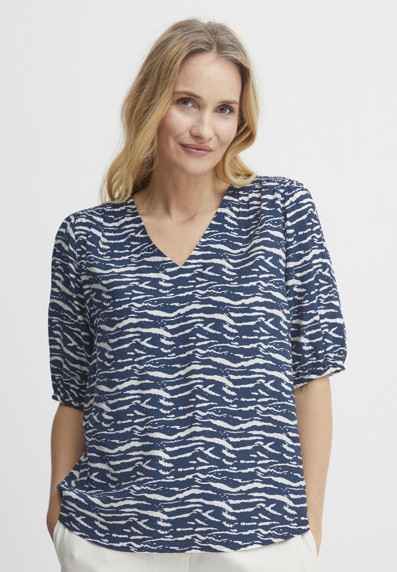 Blusa blu navy con un motivo ondulato bianco, presenta una scollatura a V e maniche a sbuffo corte, realizzata in tessuto morbido per il massimo comfort.