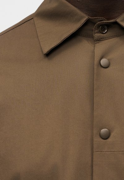 Καφέ πουκάμισο με γιακά, ματ καφέ κουμπιά τύπου snap και ένα εμφανές ραμμένο κουμπί κοντά στον γιακά.