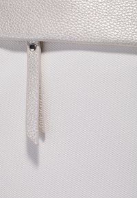 Matériau texturé en argent avec un motif subtil, doté d'une fermeture à rabat et d'un onglet suspendu, sur un fond blanc lisse.