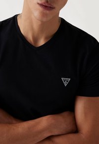 T-shirt nera a V in tessuto liscio, con un piccolo logo triangolare grigio nell'area del lato sinistro del petto. Design pulito e aderente.
