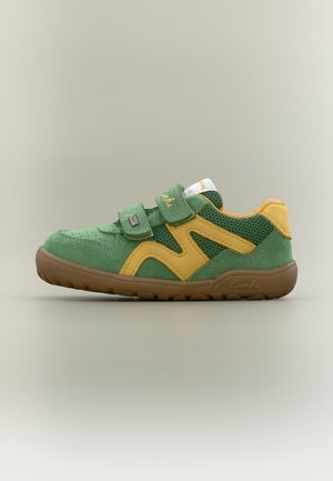 Baskets enfant vertes et jaunes avec bandes velcro et semelle en caoutchouc marron sur fond beige, vue de côté.