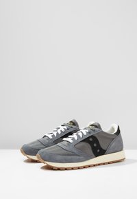 Gray athletic shoes with a mix of suede and mesh materials, white laces, a black logo, and a rubber sole with a textured bottom.