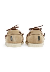 Beige Wildlederschuhe mit braunen Lederband und Branding an der Ferse. Sie verfügen über eine runde Zehenpartie und eine flache Gummisohle.