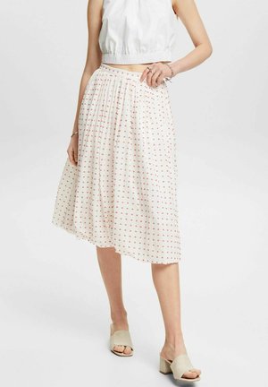 Weißer, plissierter Rock mit rotem Tupfenmuster, leichter Stoff, mittellang bis zur Wade, kombiniert mit beigen Sandalen mit klobigem Absatz und einem weißen Crop-Top.
