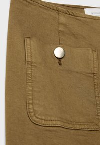 Brauner Baumwollstoff mit einer aufgesetzten Tasche, die mit einem silbernen Druckknopfverschluss ausgestattet ist. Sichtbare Nähte und eine weiche Textur verbessern das Design.