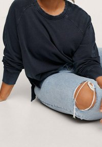 Felpa blu navy dal taglio comodo, con scollatura rotonda e maniche a raglan, abbinata a jeans azzurri chiari strappati con dettagli alle ginocchia.