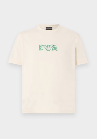 Κρεμ κοντομάνικη μπλούζα με πράσινο κείμενο "EVA" και κεντητό λογότυπο αετού στο στήθος, στρογγυλή λαιμόκοψη, επίπεδη διάταξη σε λευκό φόντο.