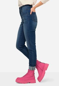 Tmavě modré skinny džíny s vysokým pasem a ohrnutými manžetami, spárované se světlými růžovými šněrovacími botami s masivní podrážkou a kontrastními akcenty.