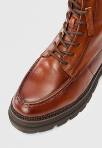 Brune lær snørebånd støvler med tykk svart såle og synlig søm på glatt, polert overdel.