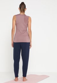 Tenue de sport composée d'un haut sans manches mauve et d'un pantalon de détente bleu marine, fabriquée à partir de tissu doux, offrant une coupe décontractée.