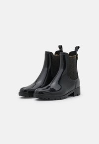 Zwarte gepatenteerde Chelsea-boots met elastische zijpanelen en gouden garenaccenten, voorzien van een gestructureerde rubberen zool en treklussen voor gemakkelijk aan- en uittrekken.