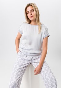 Lichtgrijs kortovertop van gladde stof, gecombineerd met witte broek met een geometrisch patroon in grijstinten. Elegante, ontspannen pasvorm.
