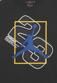 Sinine siluett korvpallurist, kes hüppab palliga suure numbri 23 kohal, kollane ruudukujuline raam mustal särgikaltsul.