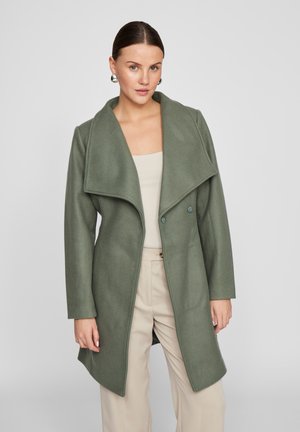 Groene wolmix mantel met een oversized kraag, dubbele knoopsluiting en lange mouwen, gecombineerd met een beige top en broek.