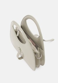 Beżowa skórzana torebka z dwoma zakrzywionymi uchwytami, zamykana na zamek, z metalowym pierścieniem jako ozdobą. Gładka faktura i usztywniony kształt.