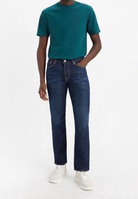 Teal bomullströja i kombination med mörkblå denimjeans. Jeansen har raka ben och en klassisk femfickdesign, bärs med vita sneakers.