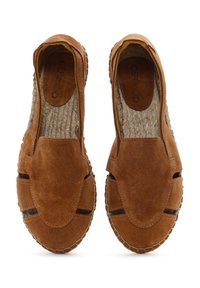 Des chaussures slip-on en daim marron avec une texture lisse, des découpes latérales ouvertes et une semelle en cuir tressé. Présente des coutures sur tout le long de la semelle.